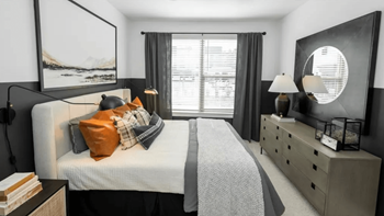 A bedroom with a large bed, a dresser, and a window with curtains.